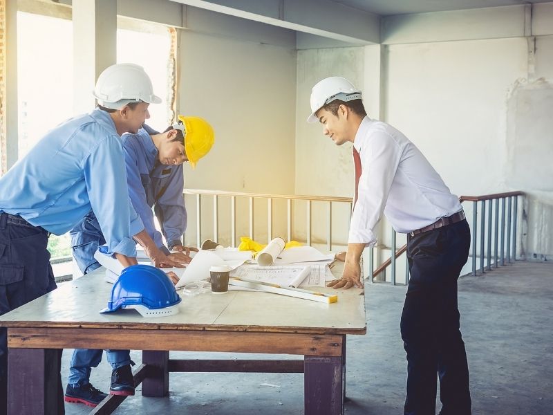 Civil engineer and construction team reviewing project plans and blueprints at a building site during the planning phase.
