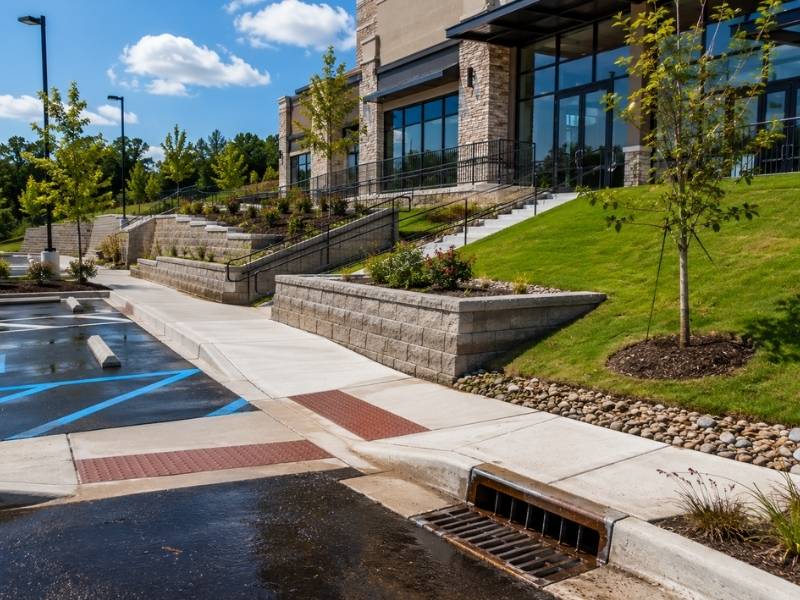 Commercial property with graded terrain, ADA-accessible walkways, retaining walls, storm drain inlet, and landscaped slopes designed for safe site accessibility and drainage.
